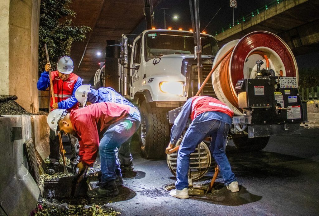 Straßenarbeiter reinigen nachts unter einer Brücke mit Maschinen die Entwässerung.