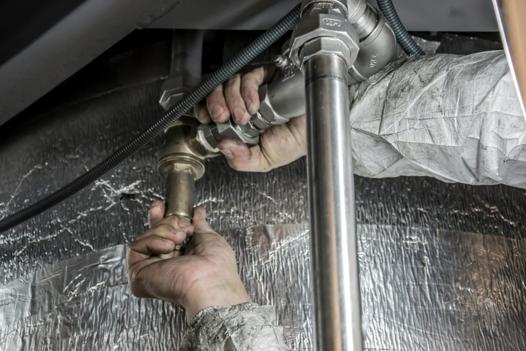 Nahaufnahme der Hände eines Installateurs beim Verlegen von Stahlrohren in Innenräumen – ein Beispiel für handwerkliches Können.