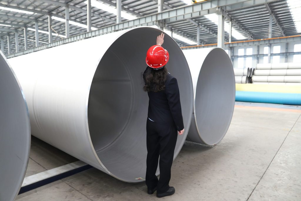 Ein Arbeiter inspiziert große Metallrohre in einer Fabrik.